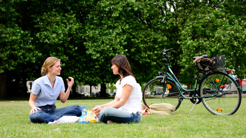 Zwei Personen sitzen in einem Park auf der Wiese.